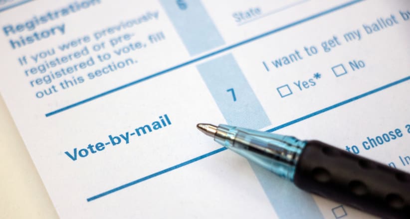 Closeup of 'Vote-by-mail' section on a voter registration form, with ballpoint pen laying on the form.