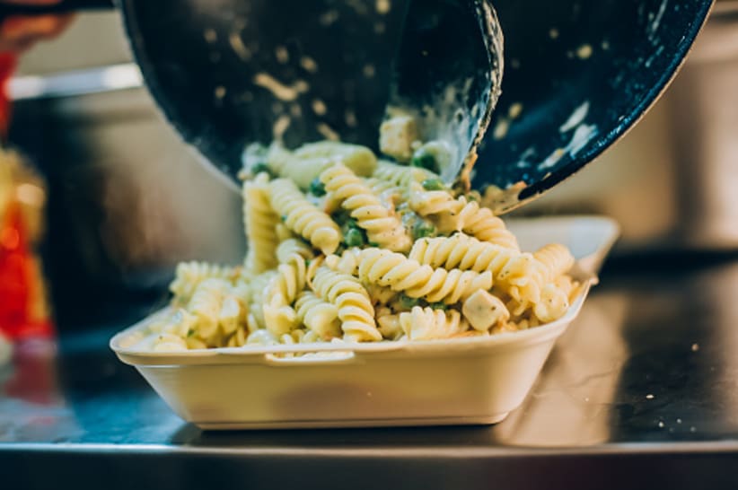 Chef cook pours spaghetti into fast food plastic delivery pack