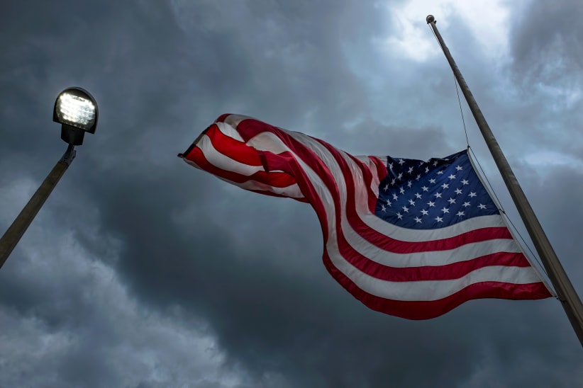 American flag at half-mast on a pole near a glowing street light in Clearwater, Florida during a storm.