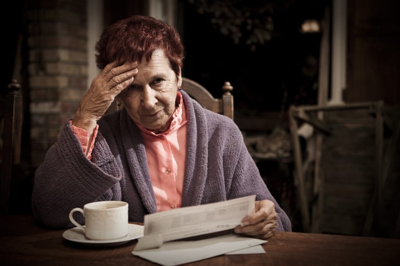 A senior woman seated at the table with a cup of coffee distressed over the costs of her bills.