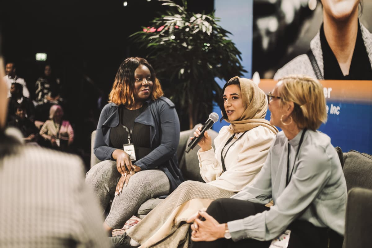 Three female panelists sitting on a couch onstage